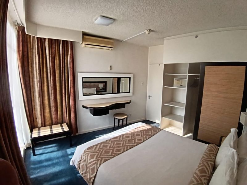 A bedroom featuring a built-in wardrobe with an integrated safe, a wall-mounted vanity, and a split-system air conditioner.
