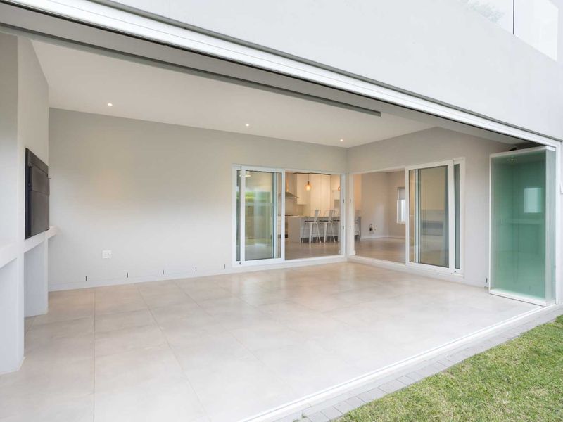 A spacious, modern covered patio featuring large sliding glass doors that open into the interior living area, complete with a built-in fireplace.