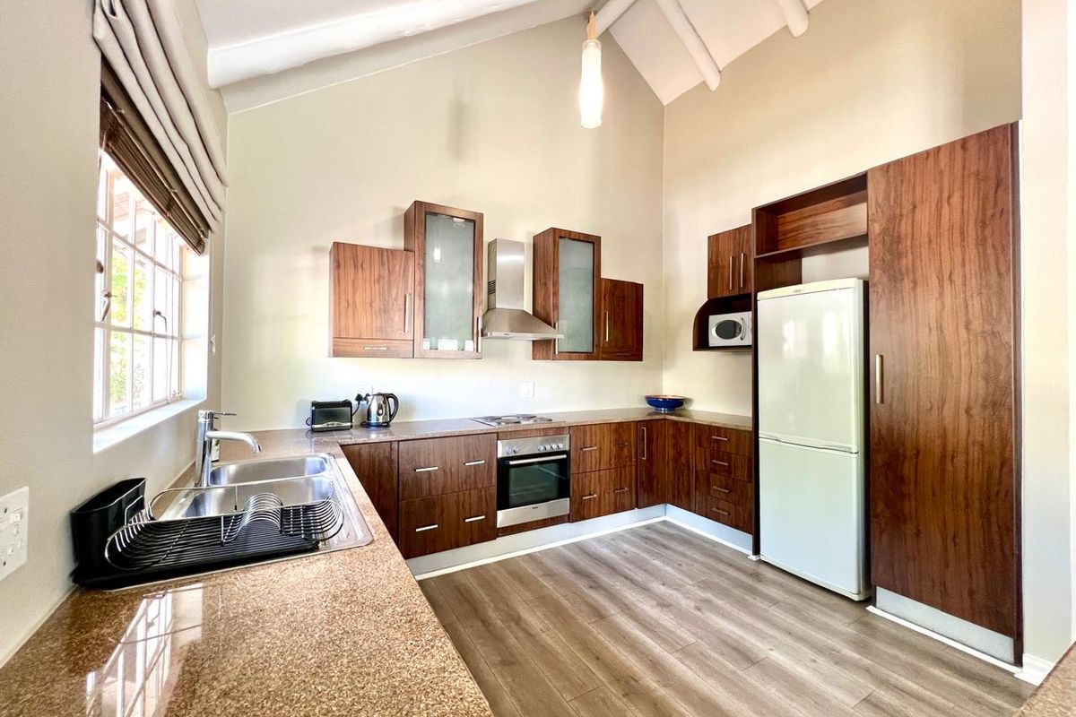 Modern kitchen featuring dark wood cabinetry, granite countertops, stainless steel appliances, and a high vaulted ceiling with exposed beams.