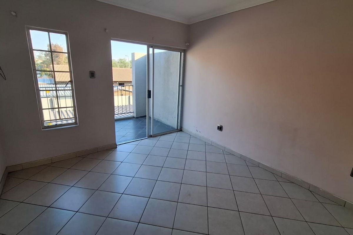 An empty living room featuring tiled flooring, a sliding glass door leading to a balcony, and a casement window, ready for personalization.