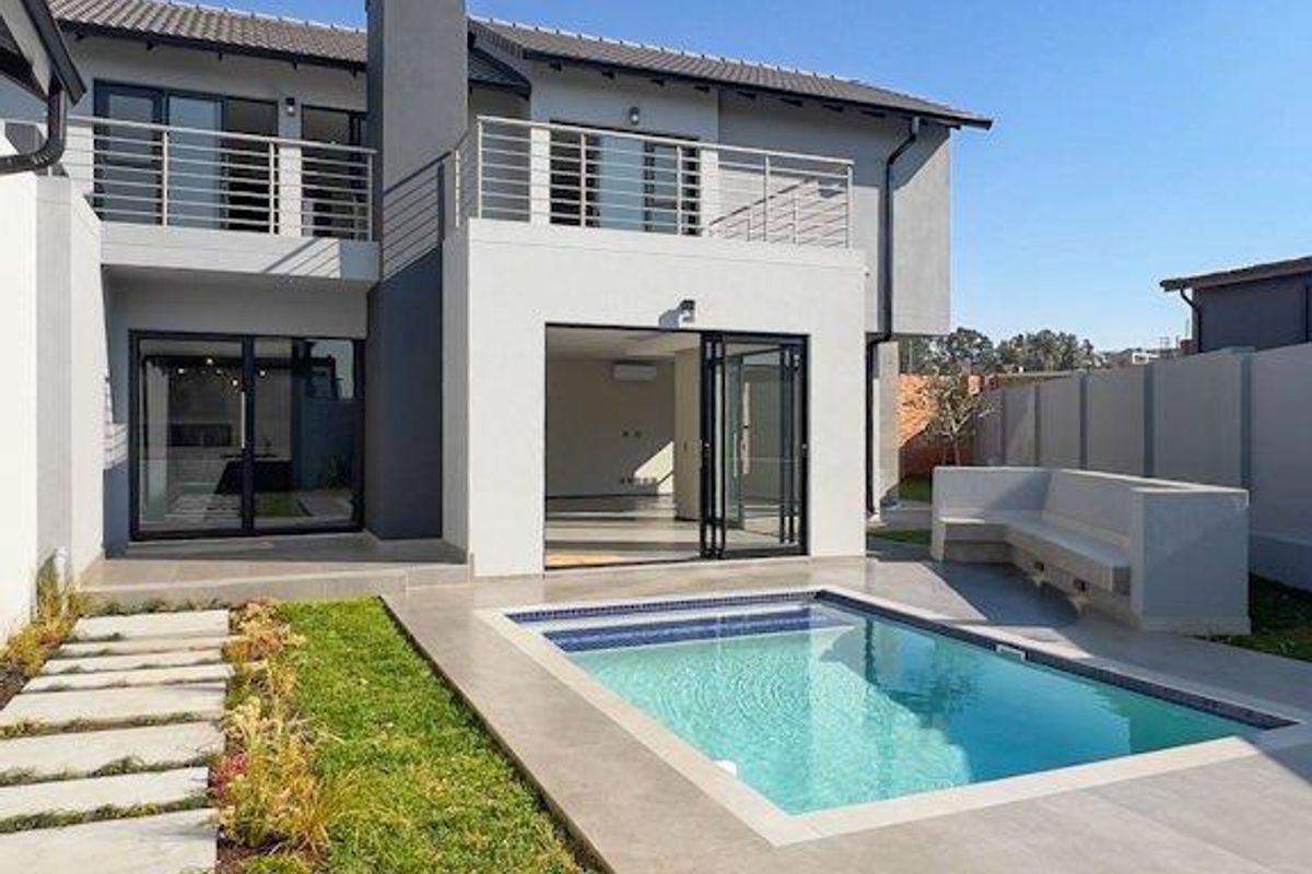 Modern rear exterior featuring a swimming pool, tiled patio area with built-in seating, and an upper-level balcony with stainless steel balustrades.