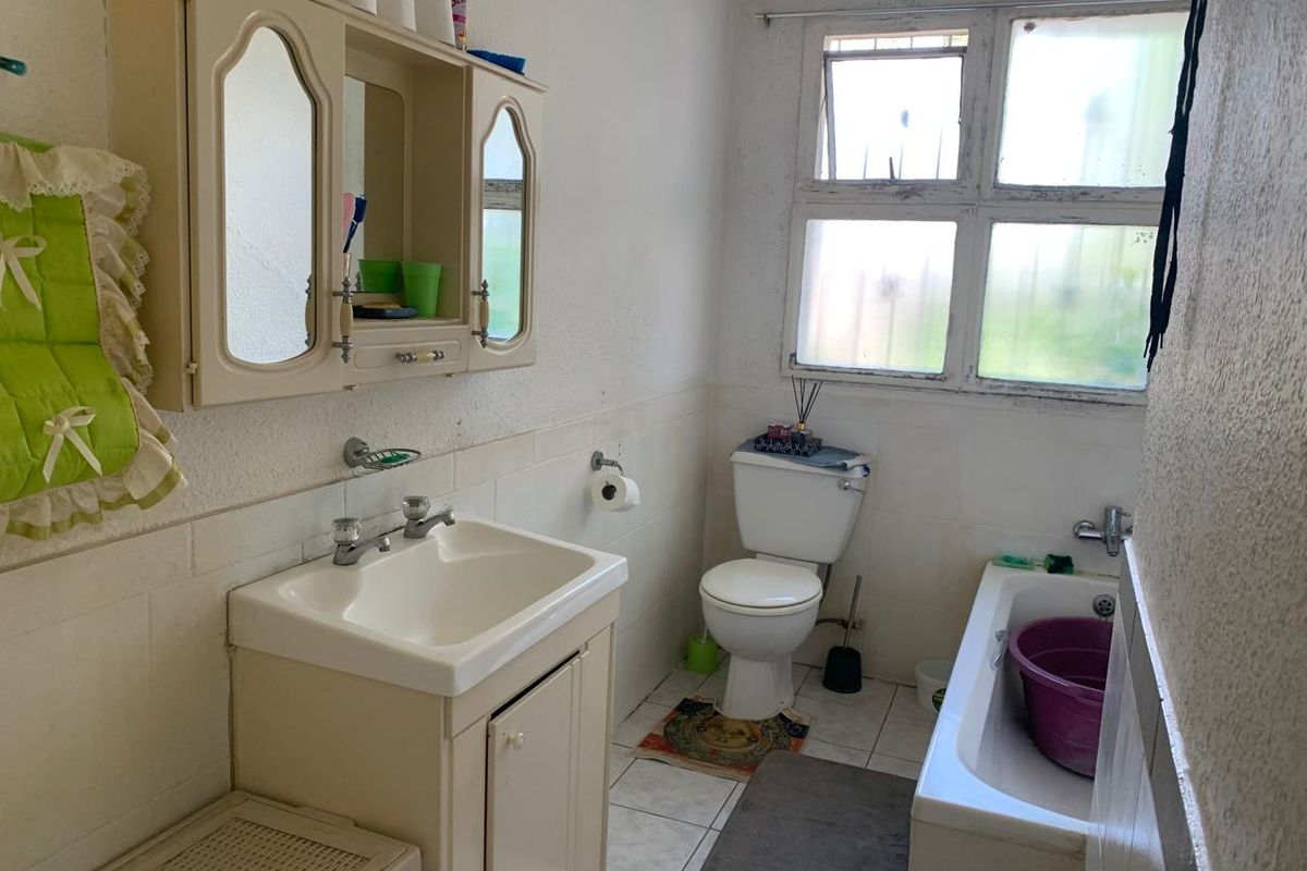 A dated bathroom featuring a vanity cabinet with integrated mirror, a standard toilet, and a bathtub with a window above.
