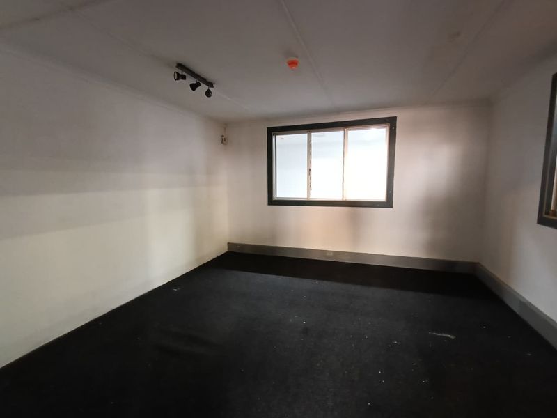 An empty, functional office space featuring dark carpet flooring, track lighting, and a single window, suitable for a variety of commercial or industrial uses.