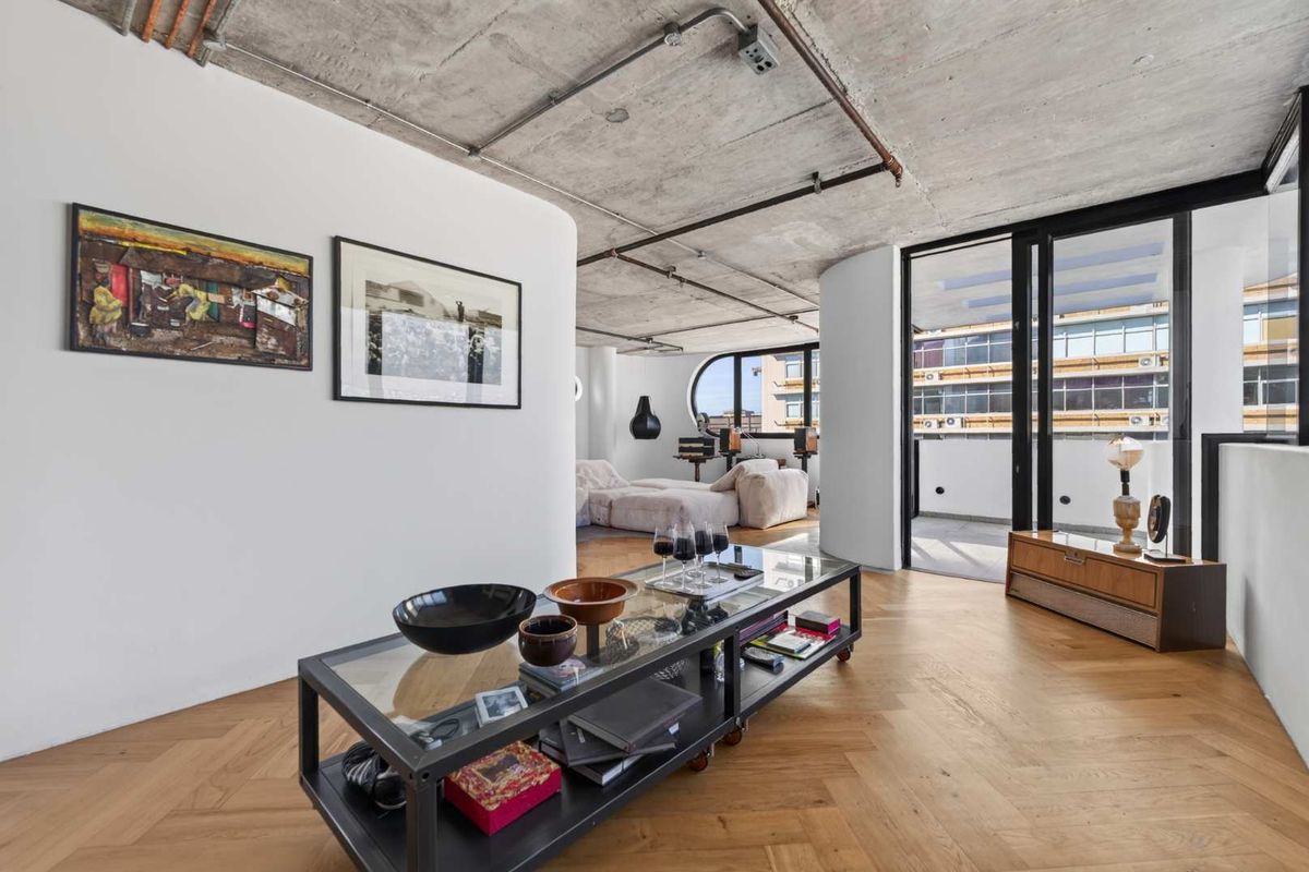 Modern living area featuring an industrial-style exposed concrete ceiling, herringbone timber flooring, and large sliding glass doors leading to a private balcony.