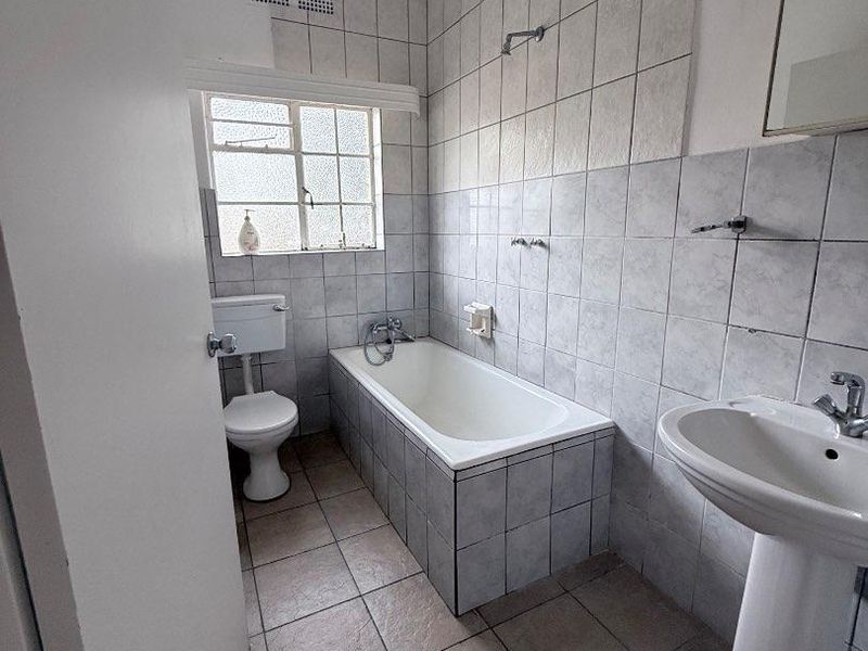 A functional bathroom featuring a pedestal basin, built-in bathtub with shower head, and tiled finishes throughout.
