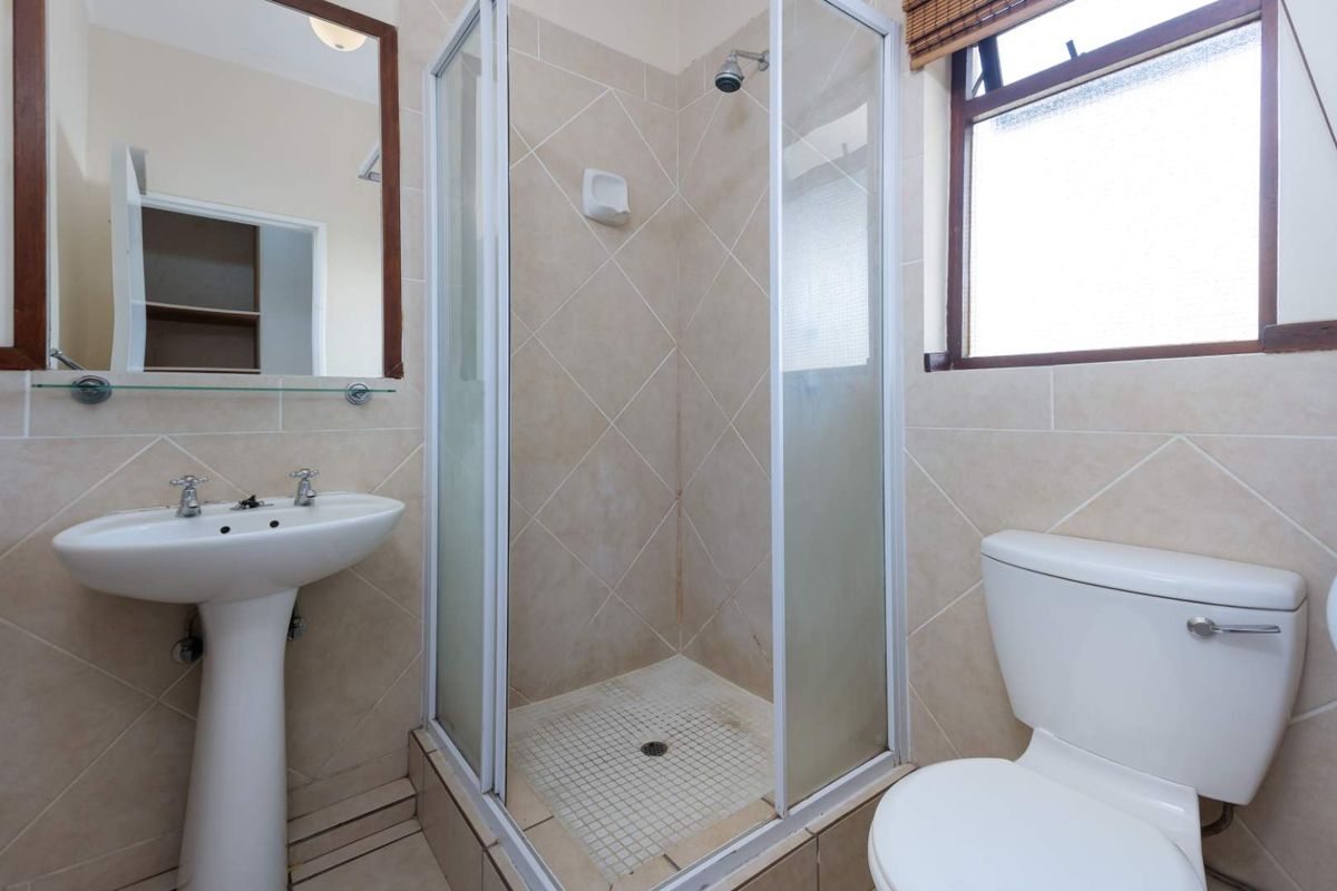 A functional bathroom featuring a pedestal sink, a corner shower enclosure with tiled walls, and a standard toilet.