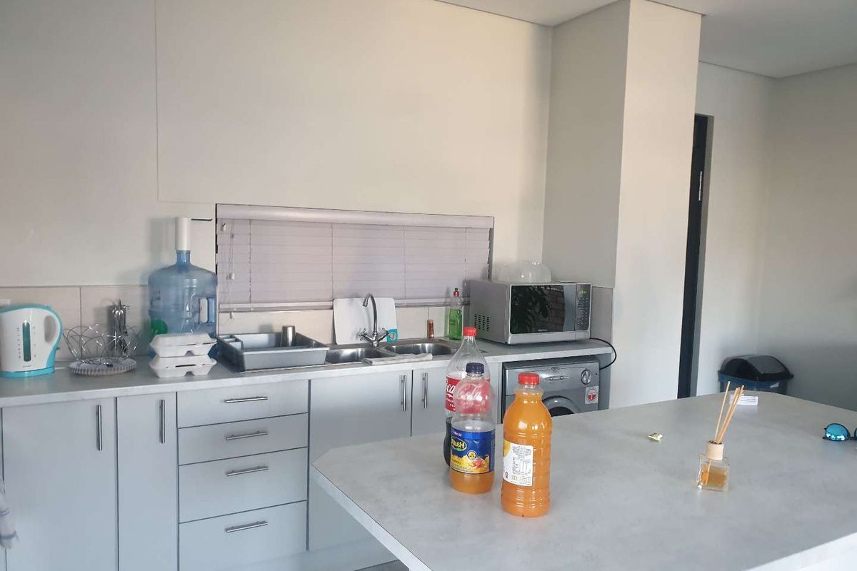 A functional kitchen featuring light-toned cabinetry, a central island, a stainless steel sink, and a built-in space for a washing machine.