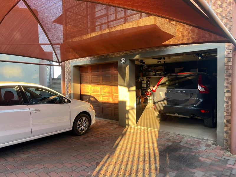 A functional garage area featuring a brick-paved driveway, a protective shade sail, and a secure sectional garage door.