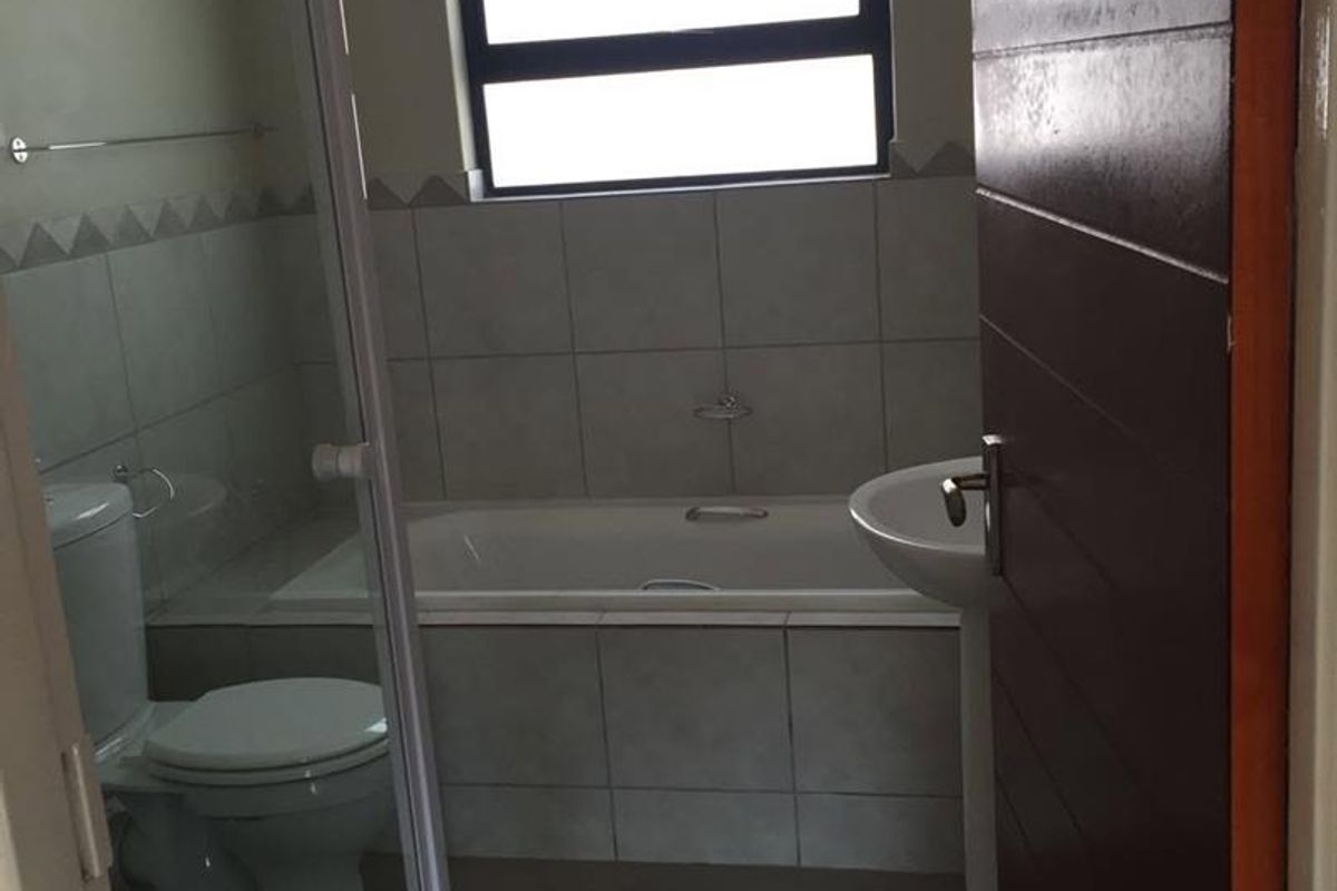 A functional bathroom featuring a shower enclosure, bathtub, and pedestal basin with neutral wall and floor tiling.