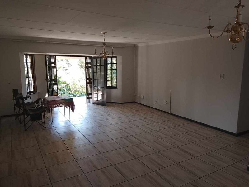 Spacious living area featuring neutral tiled flooring, classic brass chandeliers, and double french doors providing direct access to the outdoor garden space.