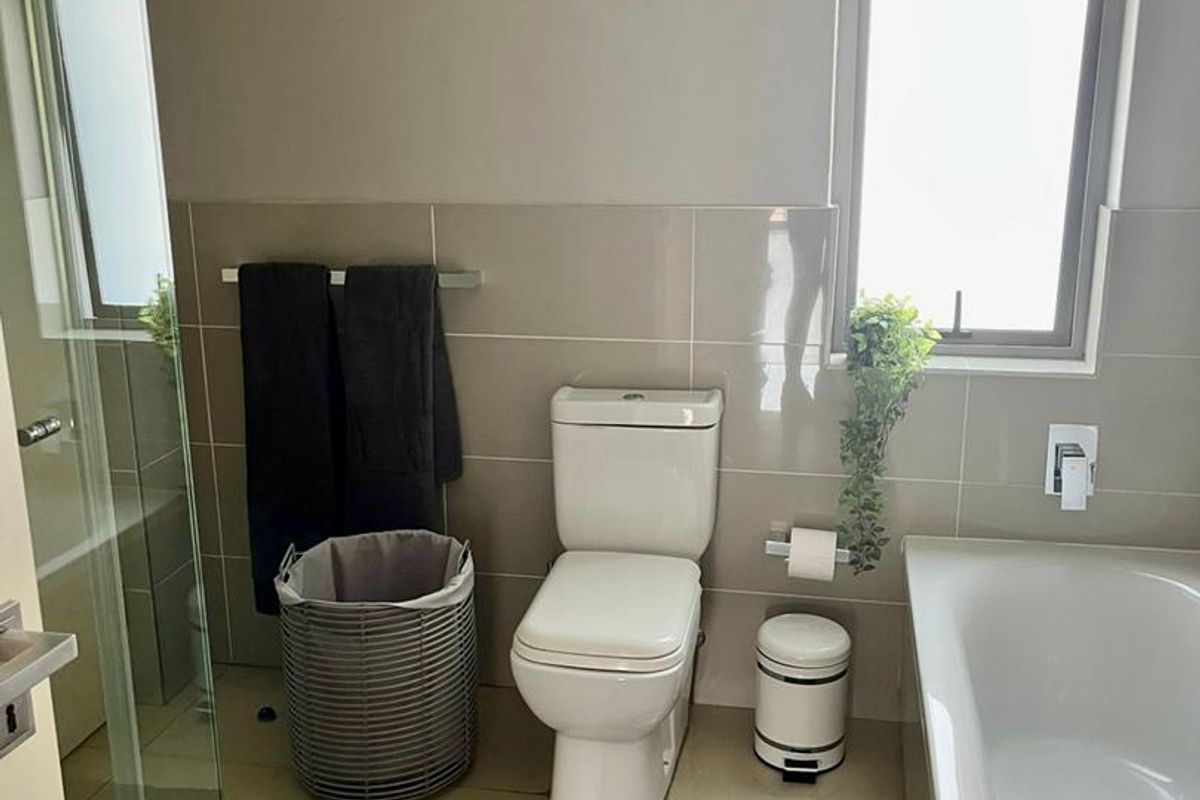 A modern bathroom featuring a bathtub, a separate glass-enclosed shower, neutral wall tiling, and a window for natural light.