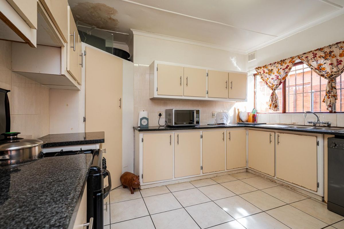 A functional kitchen featuring granite countertops, laminate cabinetry, and tiled flooring, currently showing signs of ceiling water damage and general wear.