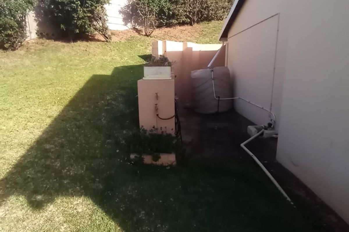 Rear exterior view of the townhouse featuring a lawn area, retaining wall, and an installed water tank with external plumbing connections.