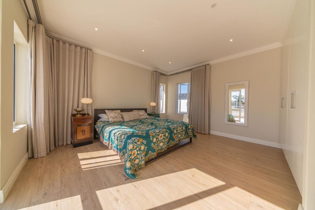 Spacious bedroom featuring light wood-look flooring, recessed ceiling lighting, and built-in wardrobe storage with a neutral color palette.