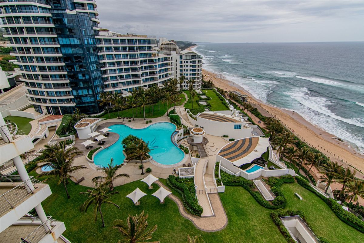 Aerial view of a luxury apartment complex featuring a large swimming pool, landscaped gardens, and direct beach access.