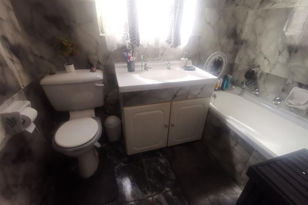 A functional bathroom featuring a vanity cabinet, washbasin, toilet, and bathtub with marble-effect wall and floor tiling.