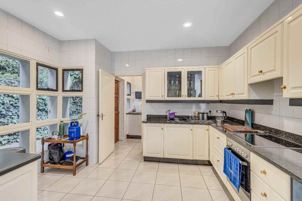A functional kitchen featuring cream-colored cabinetry, dark granite countertops, integrated oven and hob, and large windows overlooking the garden.