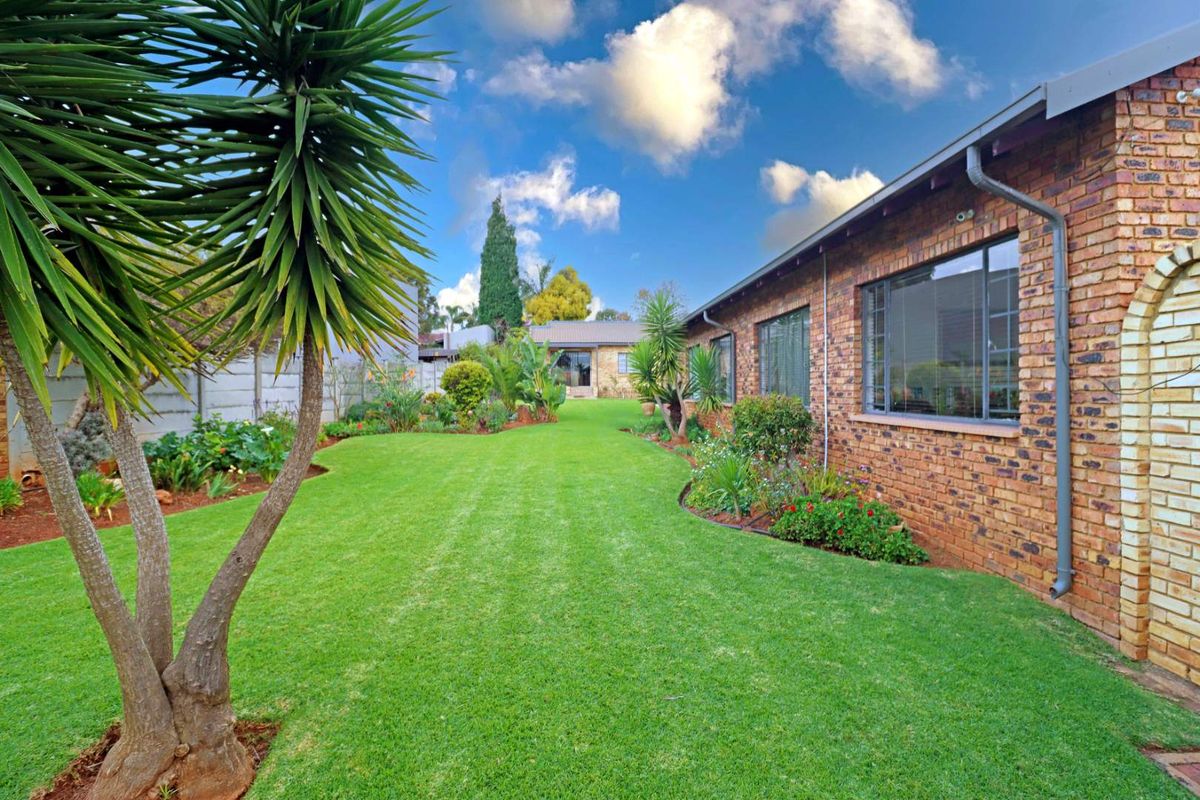 A well-maintained rear garden featuring a lush green lawn, established garden beds, and a classic face-brick exterior wall of the house.