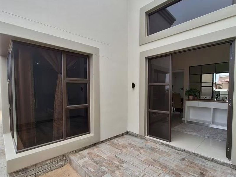 A modern covered patio area featuring tiled flooring, aluminium sliding doors, and large windows, providing a seamless transition between indoor and outdoor living spaces.