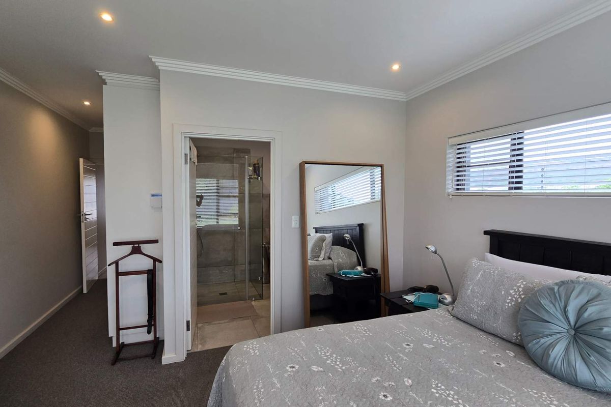 A well-maintained bedroom featuring neutral wall tones, crown molding, recessed lighting, and an en-suite bathroom with a glass-enclosed shower.