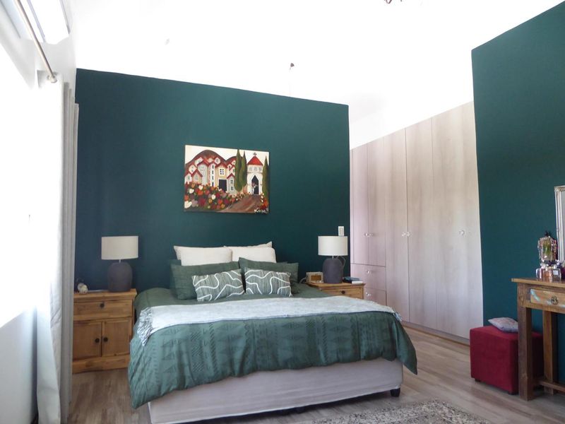 Spacious bedroom featuring dark accent wall, light wood-tone built-in cupboards, laminate flooring, and an integrated air conditioning unit.