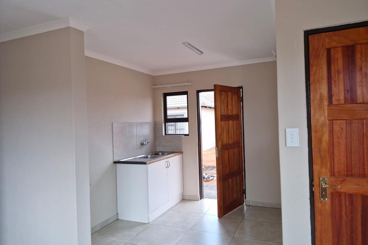 A compact kitchen area featuring a single sink unit with built-in cabinetry, tiled flooring, and direct access to the exterior.
