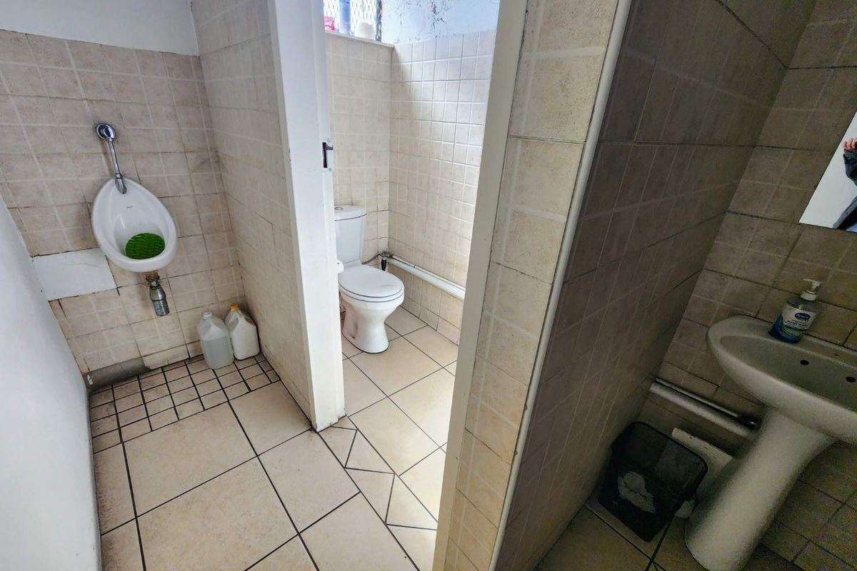 A dated commercial restroom facility featuring a wall-mounted urinal, a standard toilet, and a pedestal sink with tiled walls and flooring.