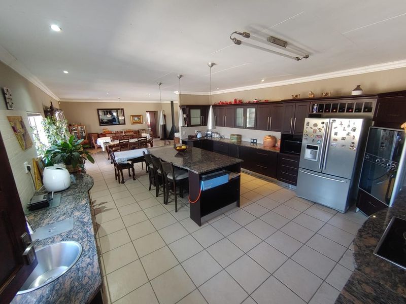 Spacious open-plan kitchen and dining area featuring dark wood cabinetry, granite countertops, a central island, and neutral ceramic floor tiles.