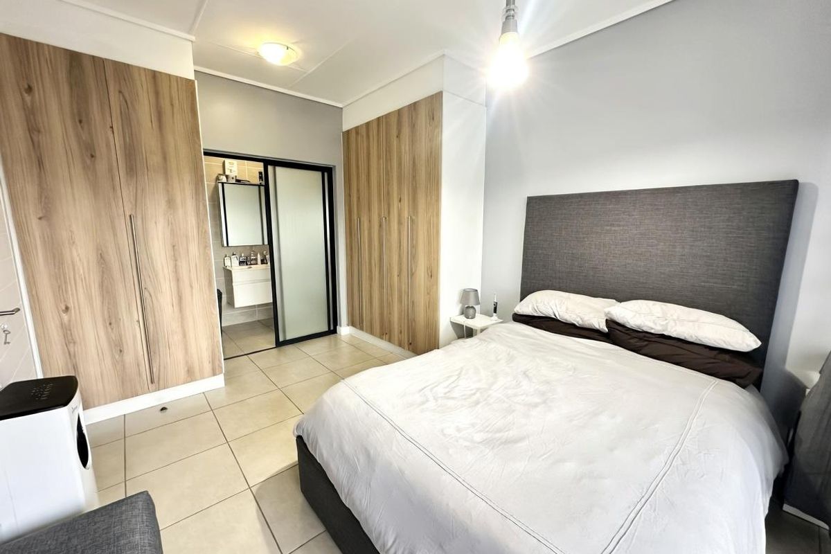 A well-maintained bedroom featuring built-in wood-finish wardrobes and an en-suite bathroom with a sliding door entry.