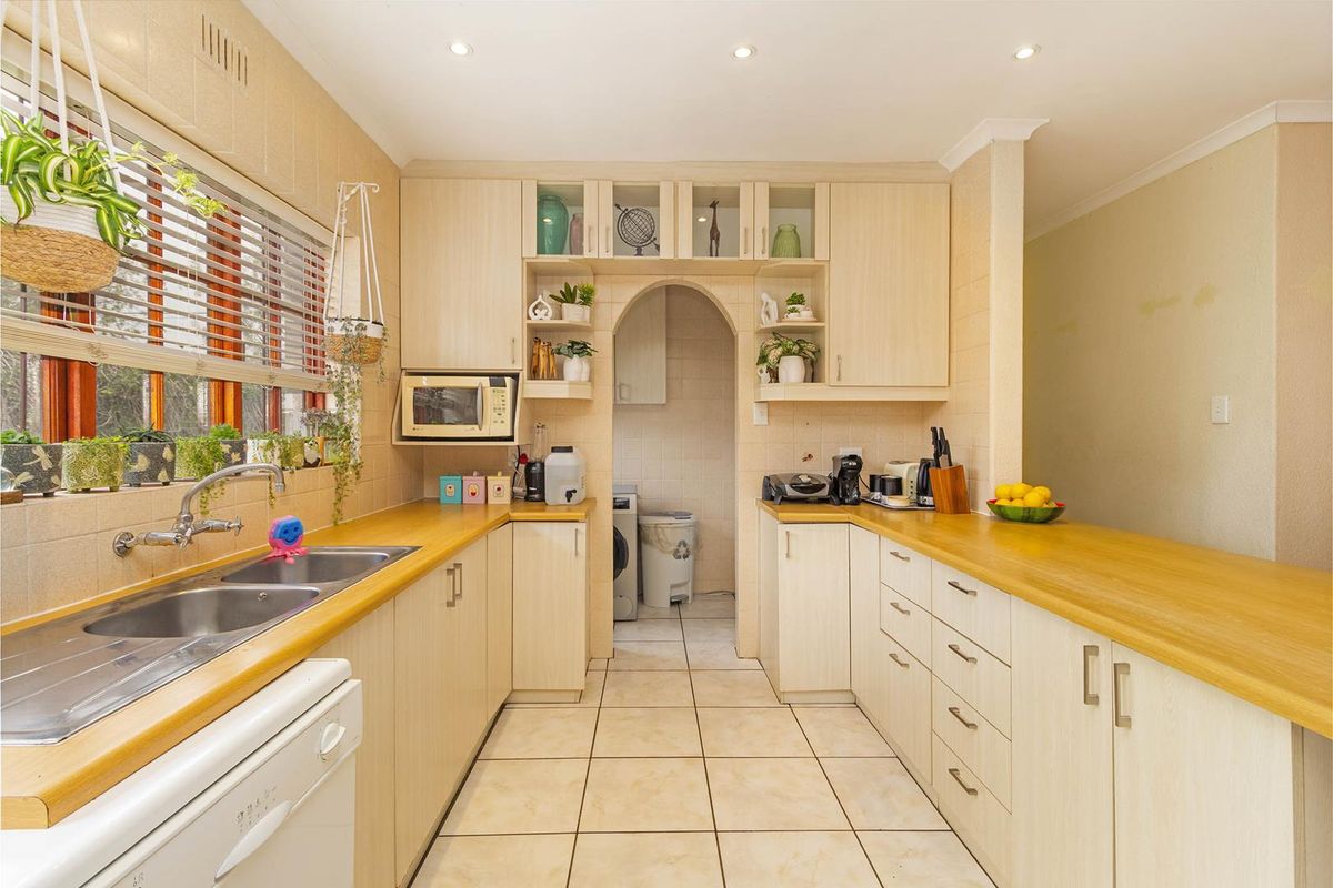 Functional kitchen featuring light-toned cabinetry, wooden countertops, tiled backsplash, and an adjoining scullery area with an arched entrance.