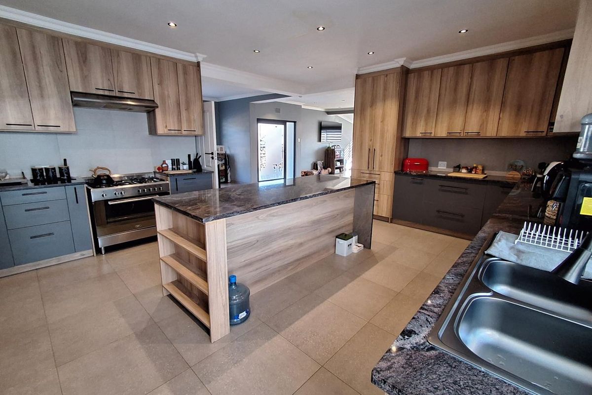 Modern kitchen featuring a central island, stone countertops, two-tone cabinetry, and a stainless steel gas stove with an integrated extractor fan.