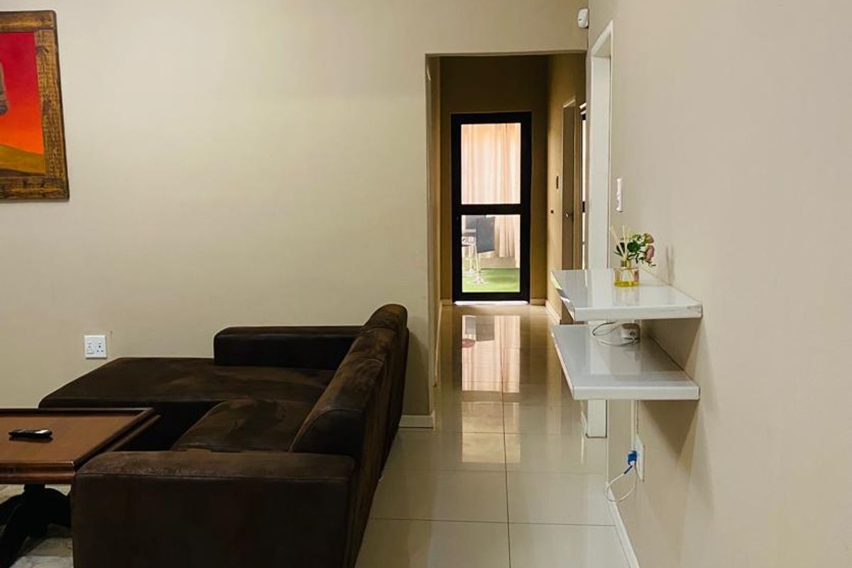 A well-maintained living area featuring neutral wall tones, polished floor tiles, and crown molding, leading to a rear access point.