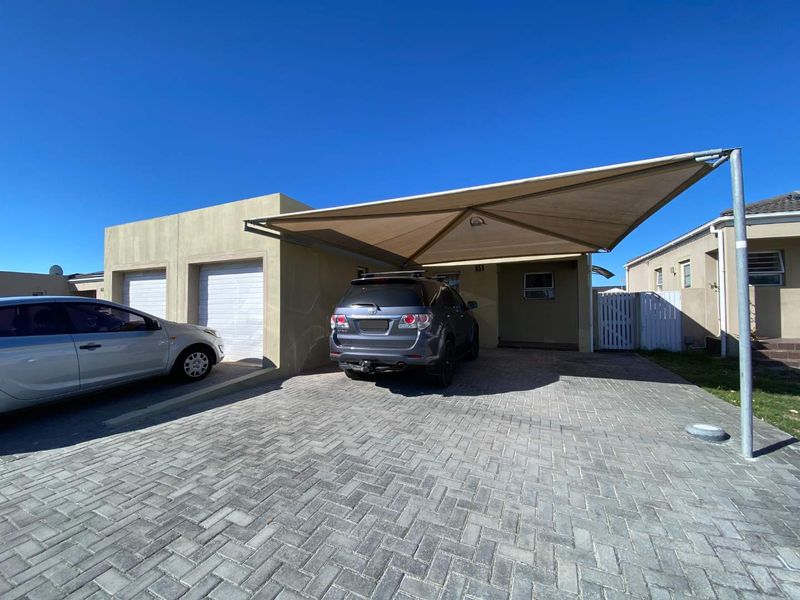 Front exterior view of the townhouse featuring a paved driveway, double garage, and a large shade sail carport for additional parking.