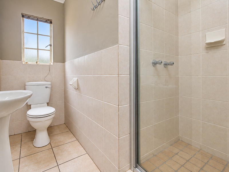 A functional bathroom featuring a pedestal basin, toilet, and a tiled shower enclosure with a glass door.