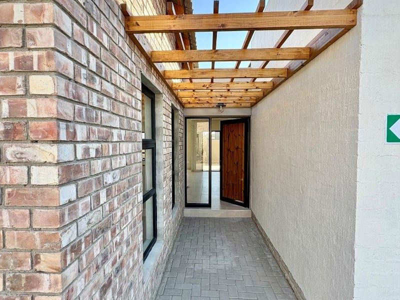 A modern entrance walkway featuring exposed brickwork, a timber pergola overhead, and a solid timber front door leading into the home.