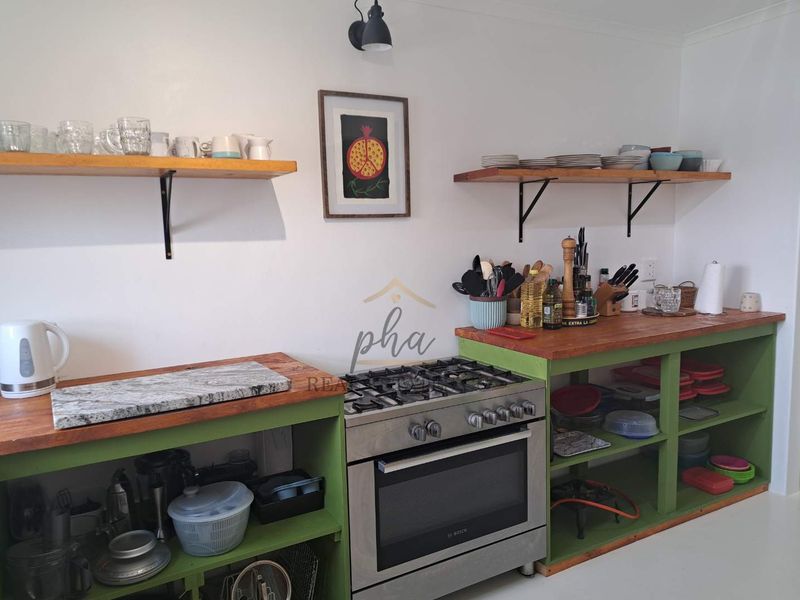 A kitchen featuring a gas stove, oven, wooden countertops, and open shelving units, providing a rustic and functional cooking space.