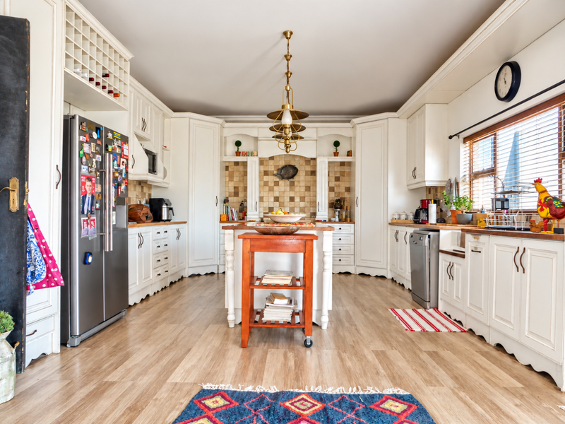 A spacious, well-lit kitchen featuring classic white cabinetry, a tiled backsplash, integrated appliances, and a central island, offering a functional and inviting culinary space.