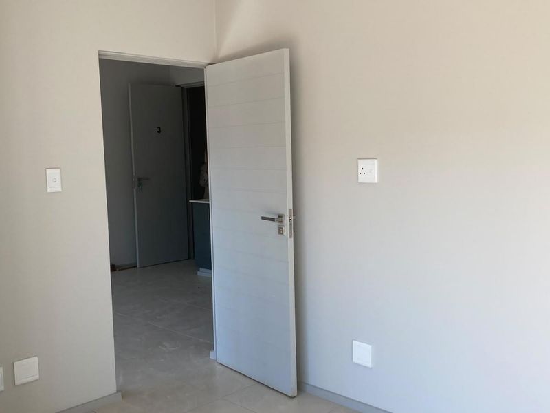A clean, empty bedroom featuring neutral wall tones, tiled flooring, and modern internal doors, providing a blank canvas for interior design.