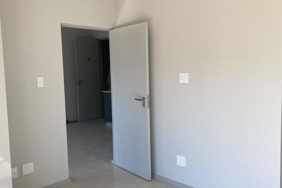 A clean, empty bedroom featuring neutral wall tones, tiled flooring, and modern internal doors, providing a blank canvas for interior design.