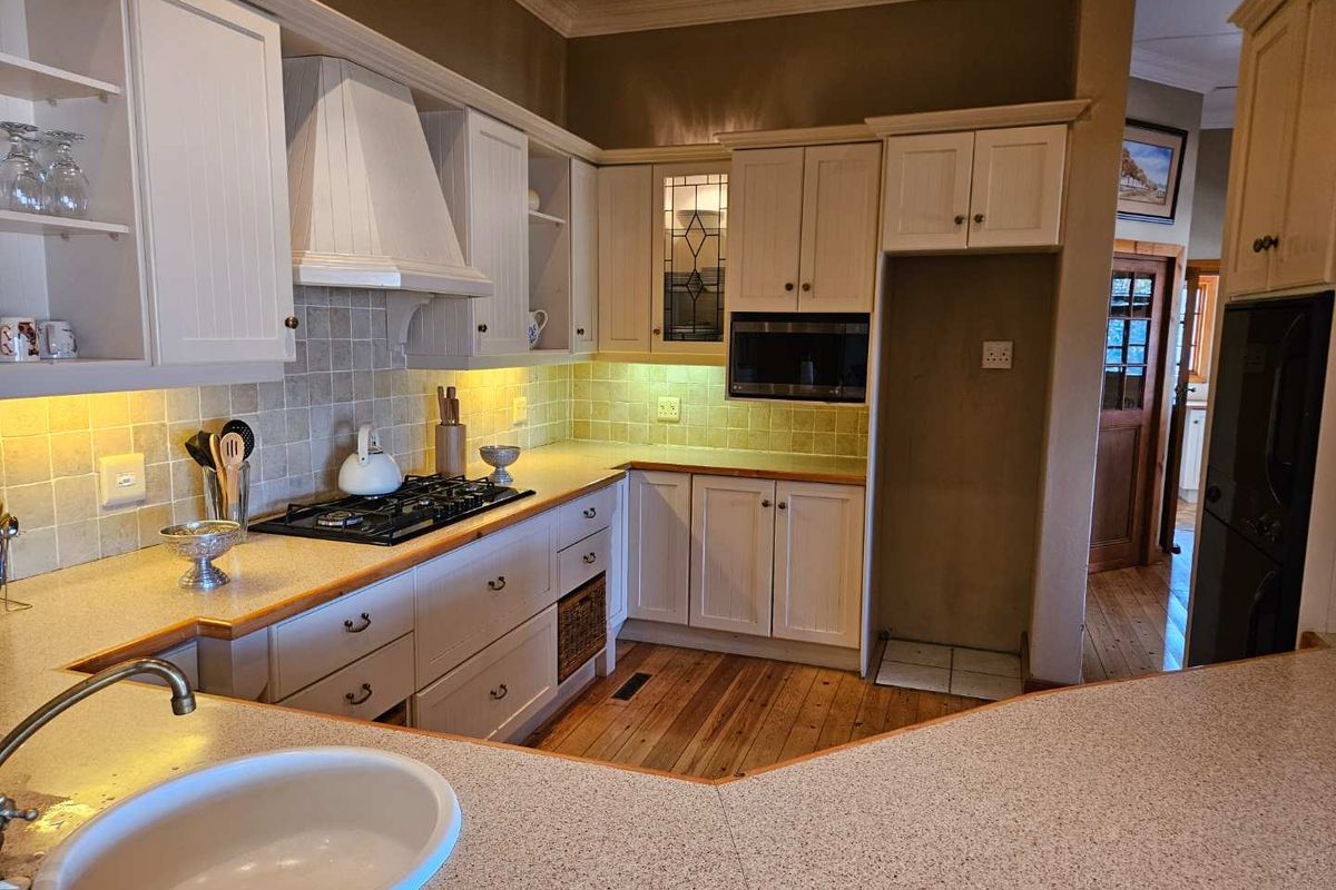 A well-maintained kitchen featuring white cabinetry, gas hob, built-in microwave, tiled backsplash, and warm hardwood flooring with ample counter space.