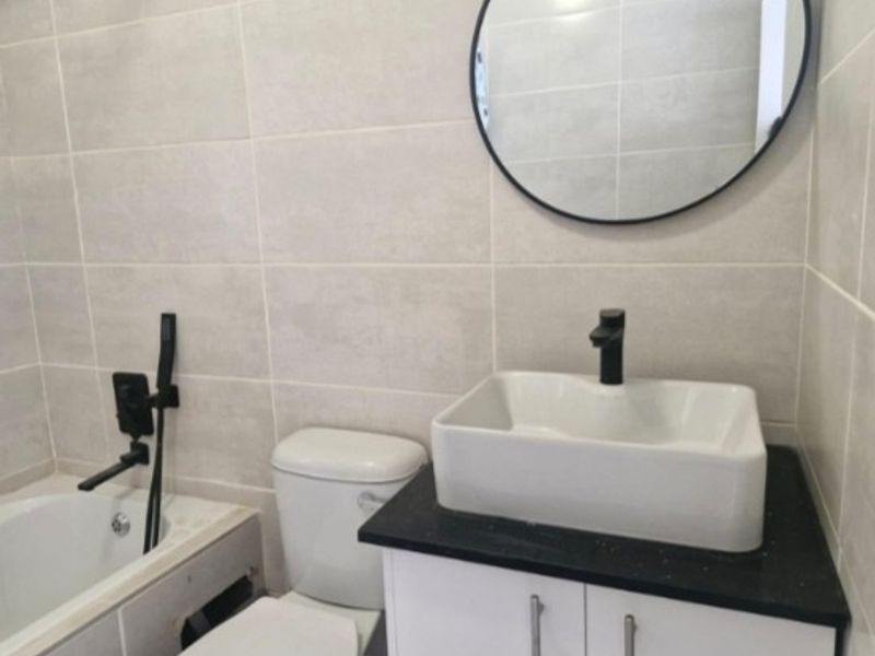 Modern bathroom featuring a vessel sink with black fixtures, a toilet, and a bathtub with tiled walls.