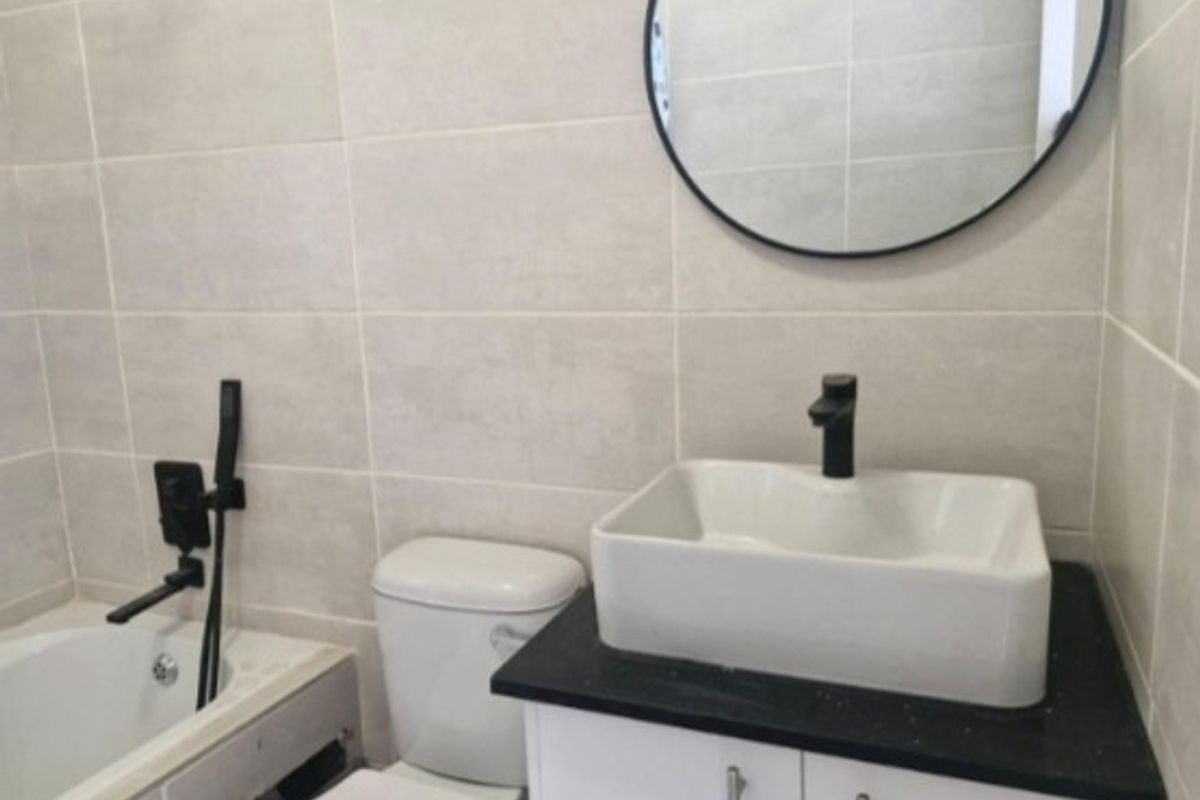 Modern bathroom featuring a vessel sink with black fixtures, a toilet, and a bathtub with tiled walls.