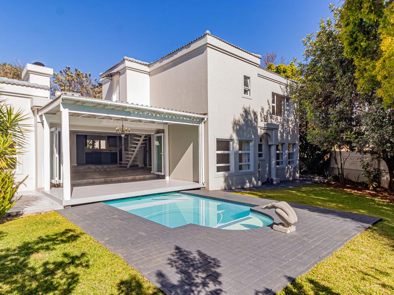 Rear view of the property featuring a swimming pool, paved deck, and a covered patio area leading into the main house.