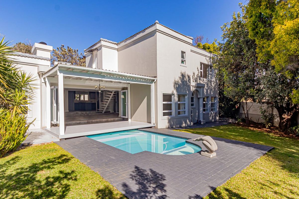 Rear view of the property featuring a swimming pool, paved deck, and a covered patio area leading into the main house.