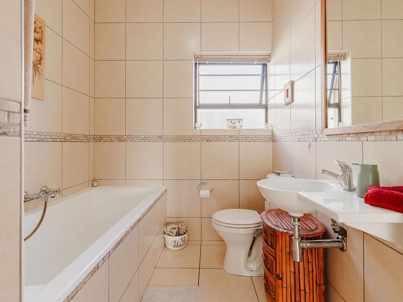 A functional bathroom featuring a bathtub, pedestal basin, and neutral wall tiling, offering a clean and practical layout.