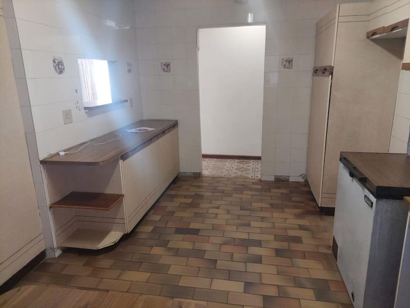 A dated kitchen featuring tiled walls, built-in cabinetry with laminate countertops, and brick-style floor tiles, offering a blank canvas for renovation.