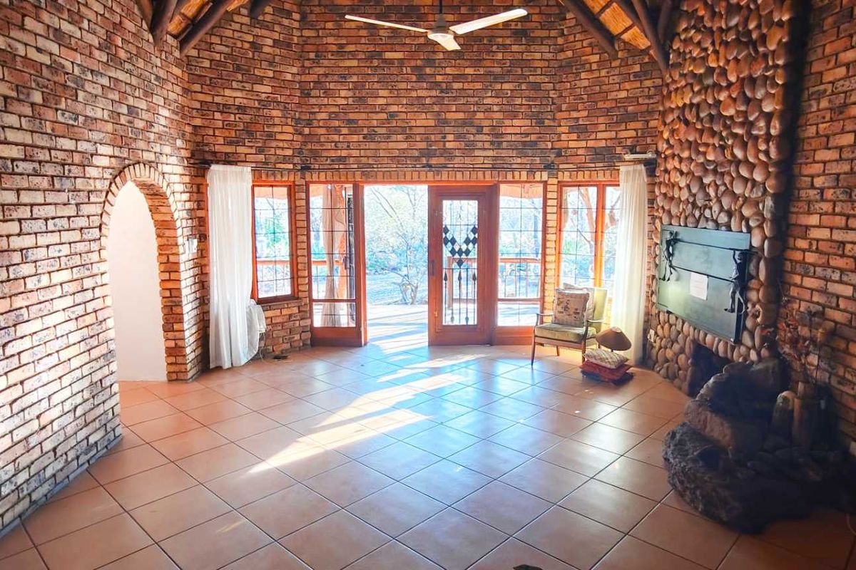 Spacious living room featuring exposed brick walls, a stone fireplace, vaulted thatched ceiling, and large glass doors opening to the outdoor area.