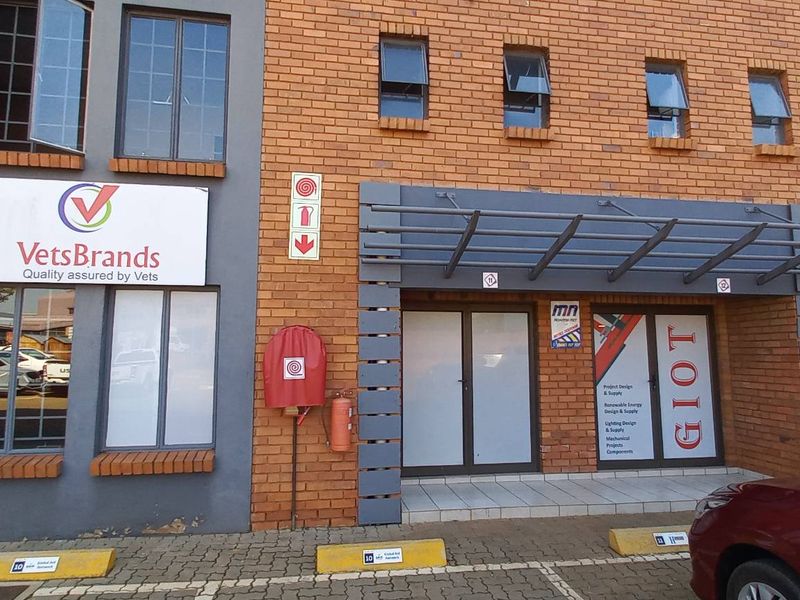 Front exterior view of a commercial industrial unit featuring face brick facade, aluminium framed windows, and a covered entrance area with paved parking.