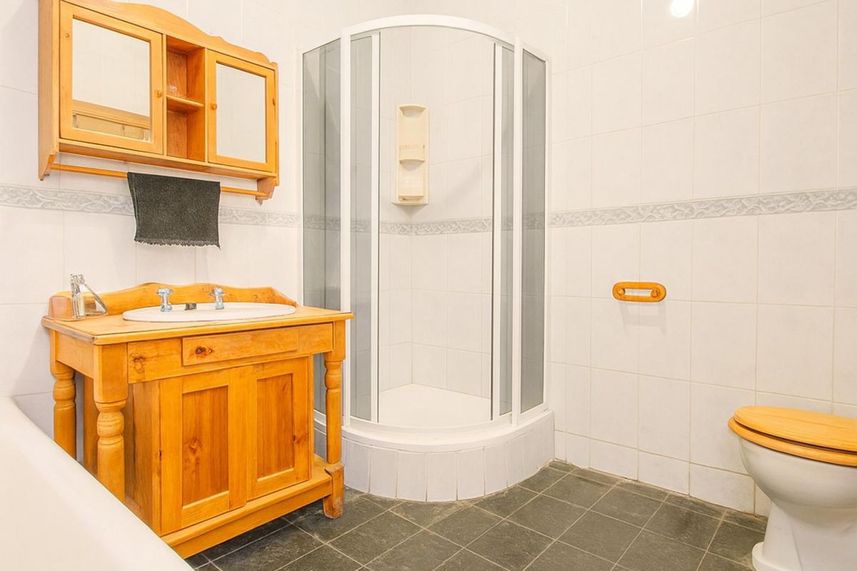 A functional bathroom featuring a corner shower enclosure, a wooden vanity unit with integrated basin, and a toilet with a matching wooden seat.
