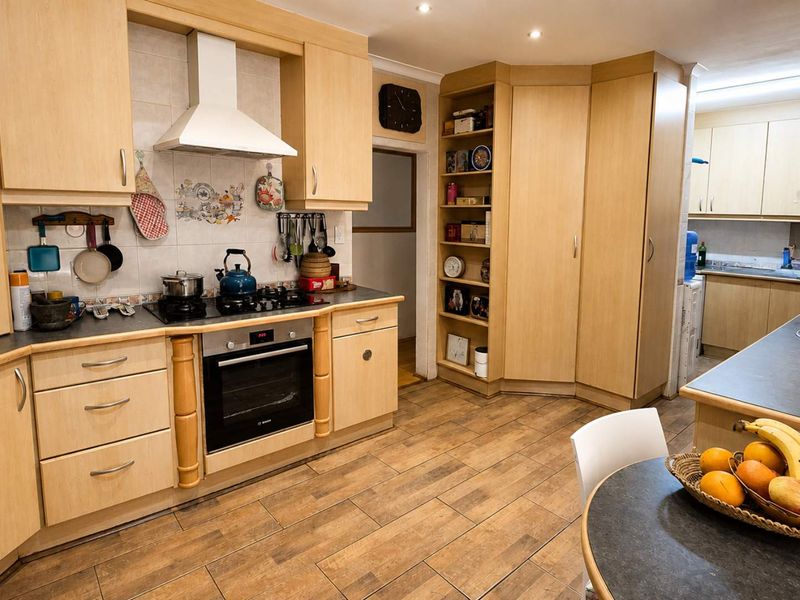 A functional kitchen featuring light wood cabinetry, built-in oven, gas hob, extractor fan, and tiled flooring with a connected scullery area.